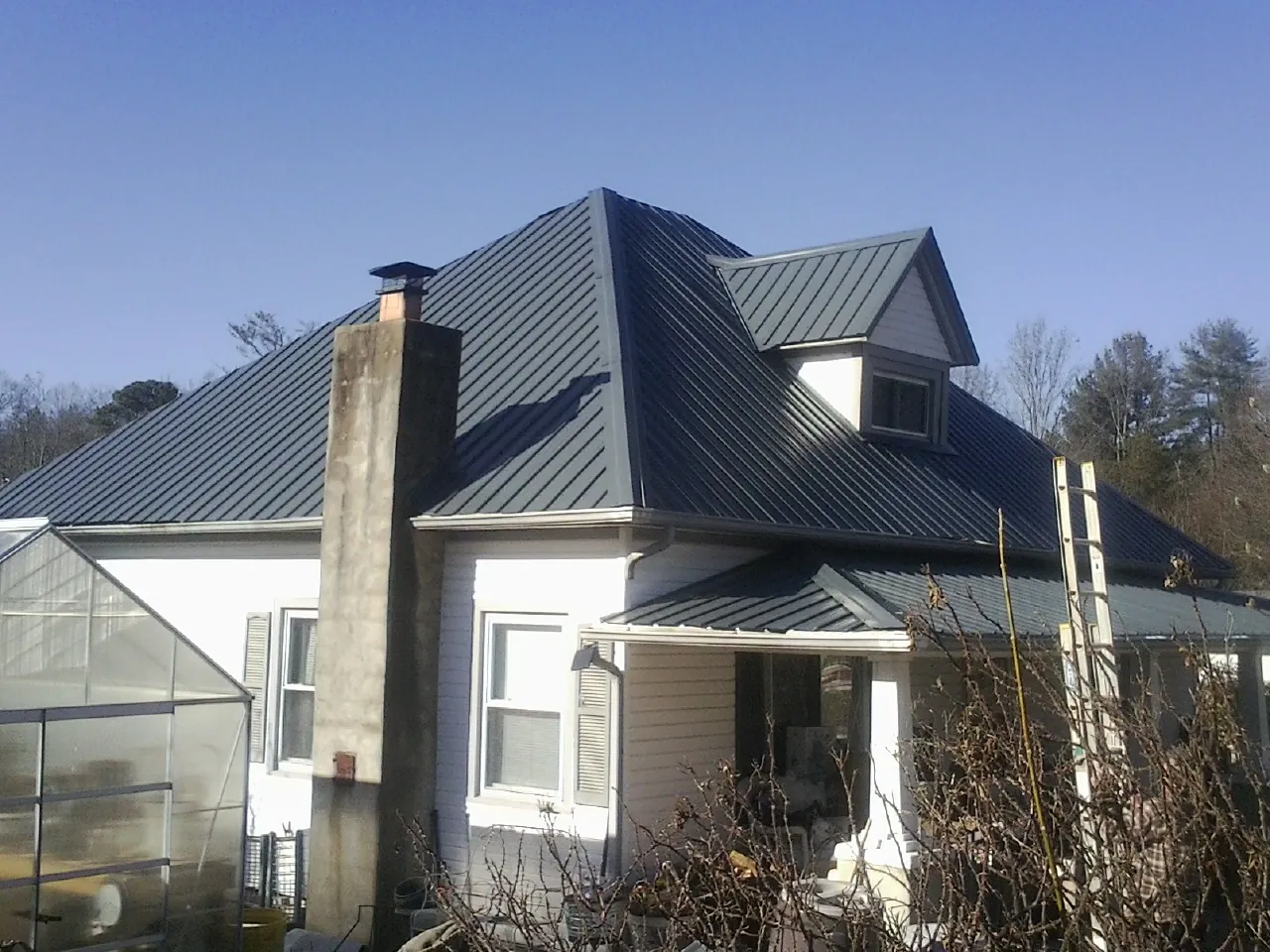 Dark blue standing seam metal roof on a white farmhouse with dormer — Slate & Tile Roof Repair by Roofing Brothers in Tarrytown