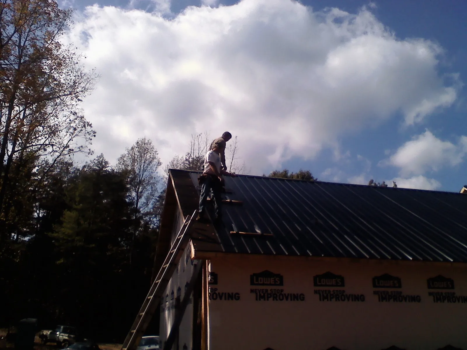 Roofer fastening dark metal panels high against a cloudy sky, from a Roof Inspection job in Tarrytown