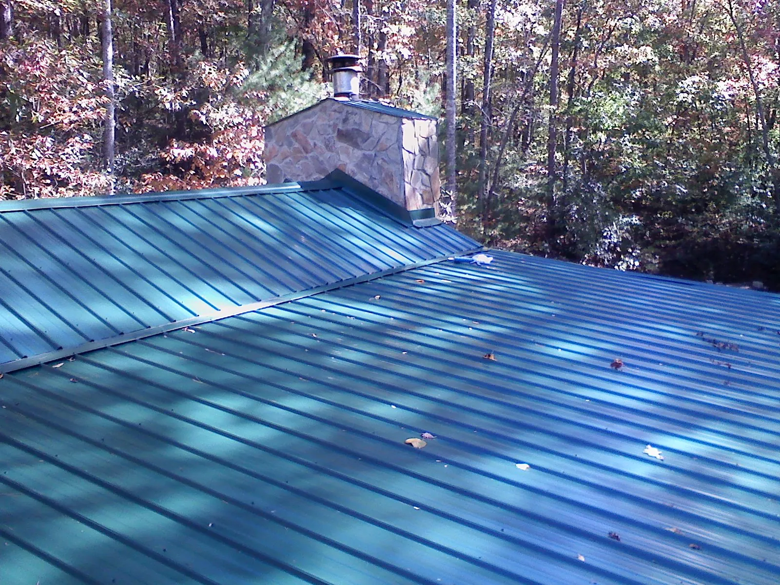 New green metal roof and stone chimney surrounded by autumn woods in Tarrytown